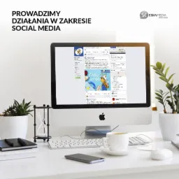 Monitor iMac wyświetlający profil na Facebooku z tekstem 'Witaj szkoło!', na biurku filiżanka kawy, klepsydra i roślina doniczkowa.