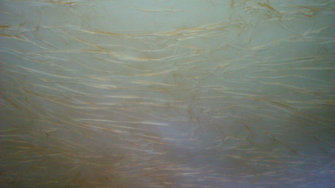 Beżowa ściana z dekoracyjną strukturą, przypominającą popękany marmur, oświetlona z góry, tworząca efekt głębi i unikalnego wykończenia wnętrza.