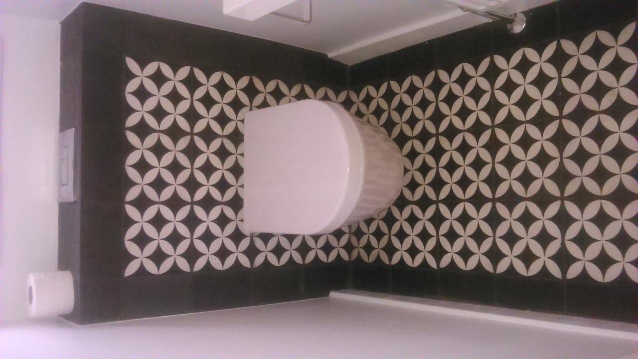 Wykończona łazienka z czarno-białymi płytkami w geometryczny wzór. Widoczny fragment toalety i rolka papieru toaletowego. Zdjęcie z góry, prezentuje detale wykończenia.