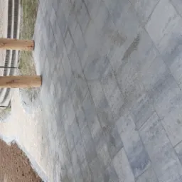 Nowa nawierzchnia z szarych, prostokątnych płyt betonowych, widoczne drewniane słupy werandy i fragment trawnika.