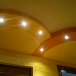 Żółto-pomarańczowy sufit z oświetleniem punktowym i dekoracyjnymi łukami, widok z dołu, fragment ściany z fakturą i stolarki okiennej.