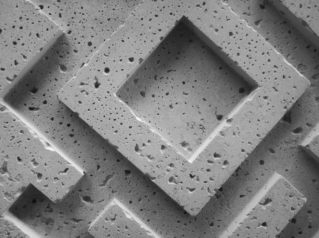 Szare, porowate płyty betonowe ułożone warstwami tworzące wzór rombów z pustymi środkami, widoczne z bliska pod kątem.
