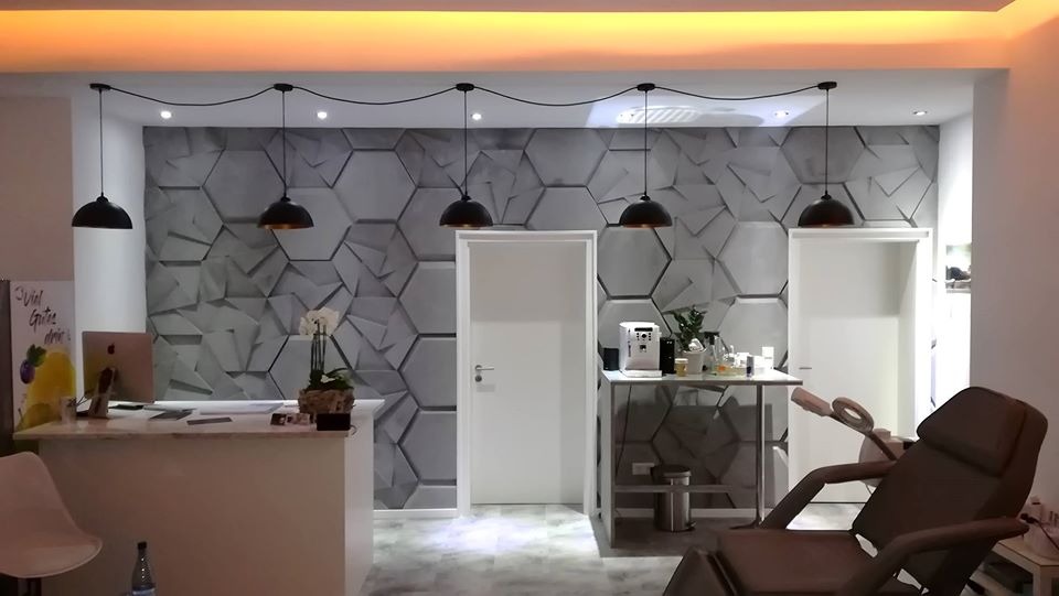 Recepcja salonu kosmetycznego w Bielsku-Białej z panelami 3D o strukturze plastra miodu na ścianie, oświetlona wiszącymi lampami z czarnymi kloszami i jasnym sufitem.