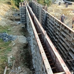 Erbud Robert Strus - Szalunki zbrojeniowe przygotowane do zalania betonem, widok z góry na wykop, w tle zieleń i dwóch pracowników budowlanych.