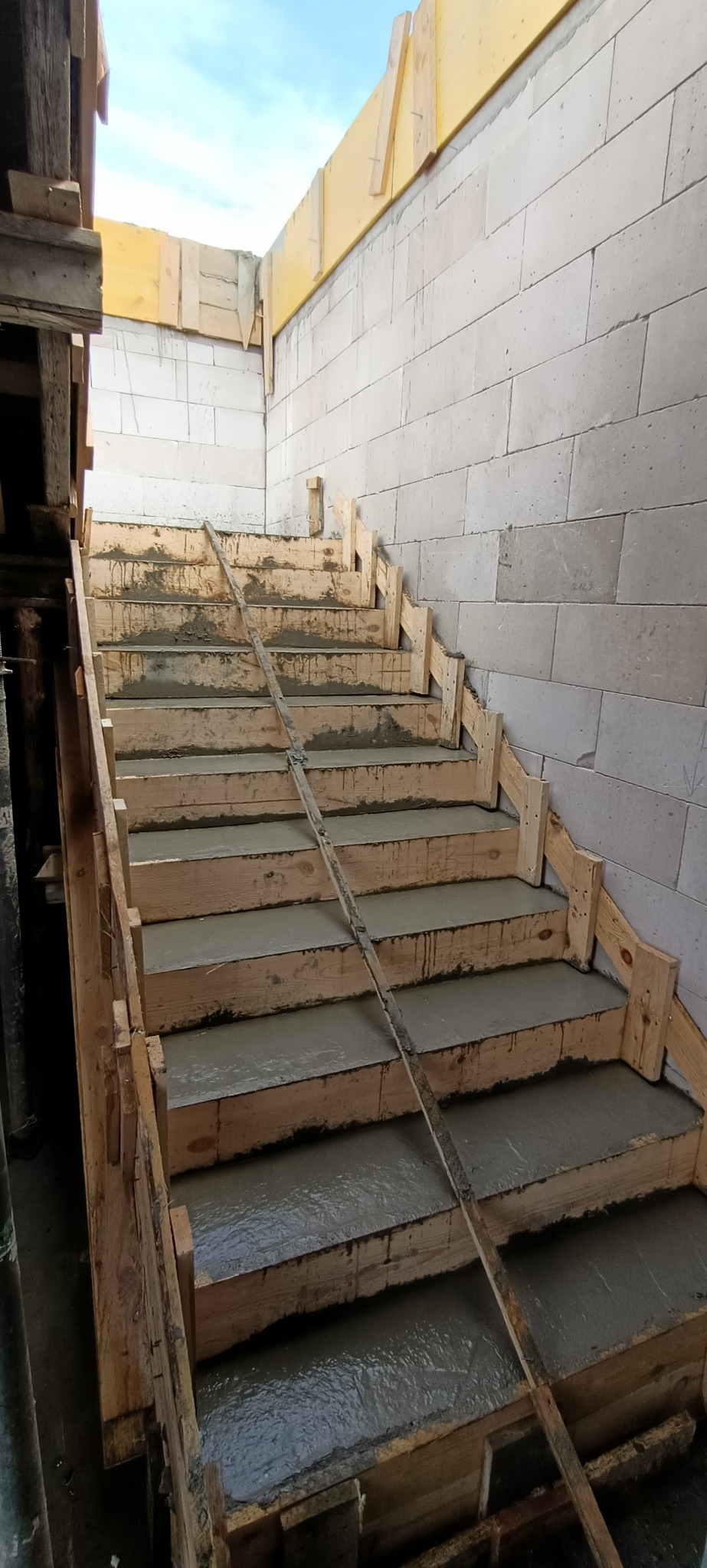 Wypełnione betonem stopnie schodów w drewnianym szalunku, widoczne ściany z bloczków gazobetonowych.