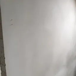 Gładka, świeżo nałożona jasna powłoka na ścianie, widoczne ślady po szpachlowaniu, fragment surowego muru i schodów w dolnej części kadru.