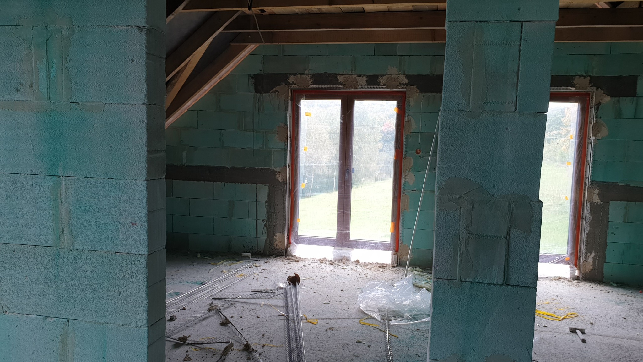 Wnętrze surowego budynku z bloczków, przygotowane do tynkowania maszynowego, widoczne profile i okna zabezpieczone folią.