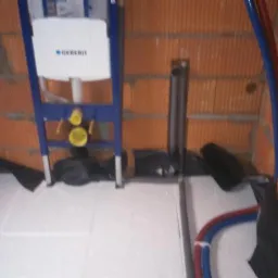 Montaż stelaża podtynkowego Geberit na ścianie z cegły, widoczne rury instalacji wodnej i kanalizacyjnej, oraz izolacja pod ogrzewanie podłogowe.