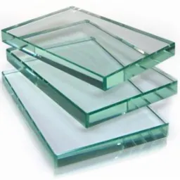 Stos tafli szkła o gładkich krawędziach, ułożonych warstwowo, z delikatnym zielonkawym odcieniem, na jasnym tle. Widoczne refleksy świetlne.