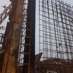 Konstrukcja zbrojeniowa ściany w trakcie budowy, widoczne elementy szalunku i przewody, na ziemi leży śnieg.