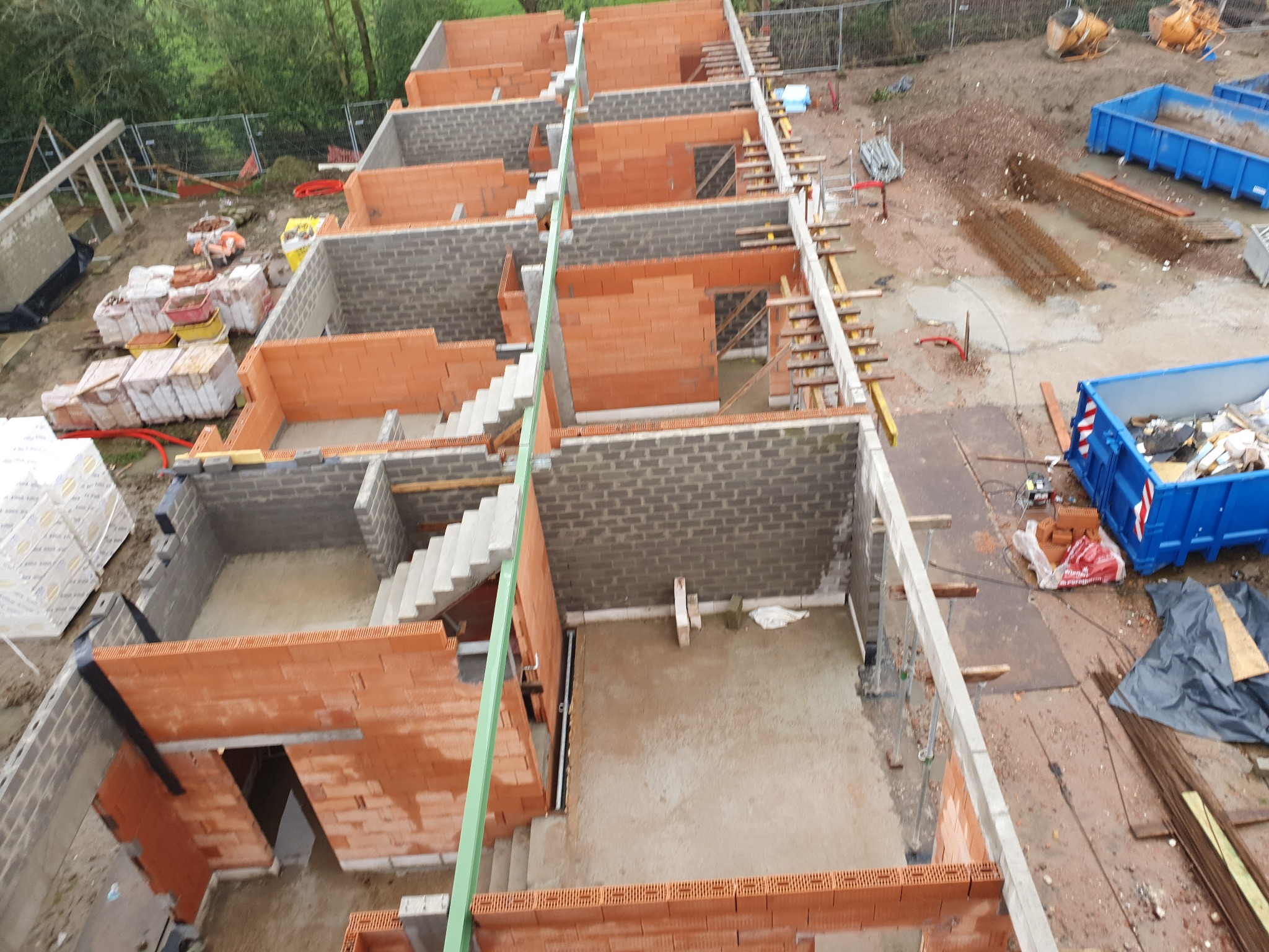 Budowa szeregu domów w stanie surowym, widok z góry, widoczne cegły ceramiczne, betonowe bloczki i elementy konstrukcyjne schodów.