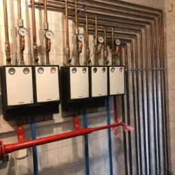 Rozbudowana instalacja grzewcza z wieloma rozdzielaczami i rurami miedzianymi, widoczne manometry, zrealizowana w Nowym Mieście nad Wartą.