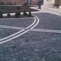 Eleganckie schody i podjazd z ciemnej kostki brukowej z białymi liniami dekoracyjnymi, otoczone zielenią w Drawsku.