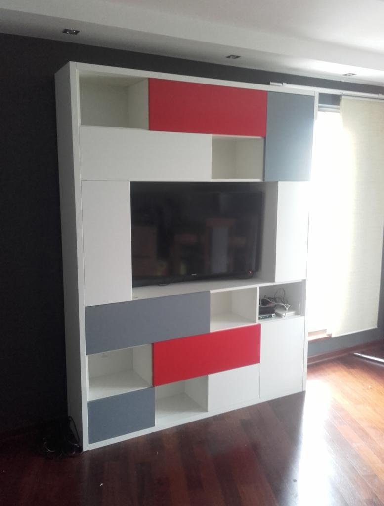 Biała, modułowa szafa w salonie z czerwonymi i szarymi akcentami, wbudowana pod telewizor, widoczna podłoga z ciemnego drewna.