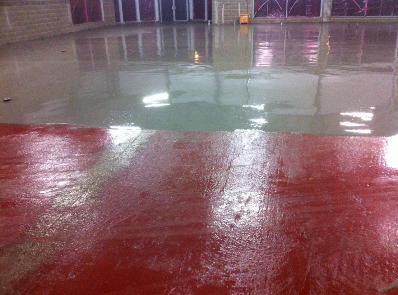 Świeżo wylana, dwukolorowa posadzka w hali przemysłowej, z widocznymi refleksami światła i fakturą mokrej powierzchni.