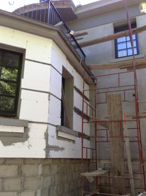 Ocieplanie elewacji domu styropianem, widoczne rusztowanie i fragment balkonu z metalową barierką.