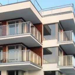 Nowoczesny budynek mieszkalny z balkonami z balustradami ze szkła i ramami okiennymi w kolorze srebrnym, widok z dołu pod kątem na boczny narożnik budynku, z drewnianą okładziną między oknami.