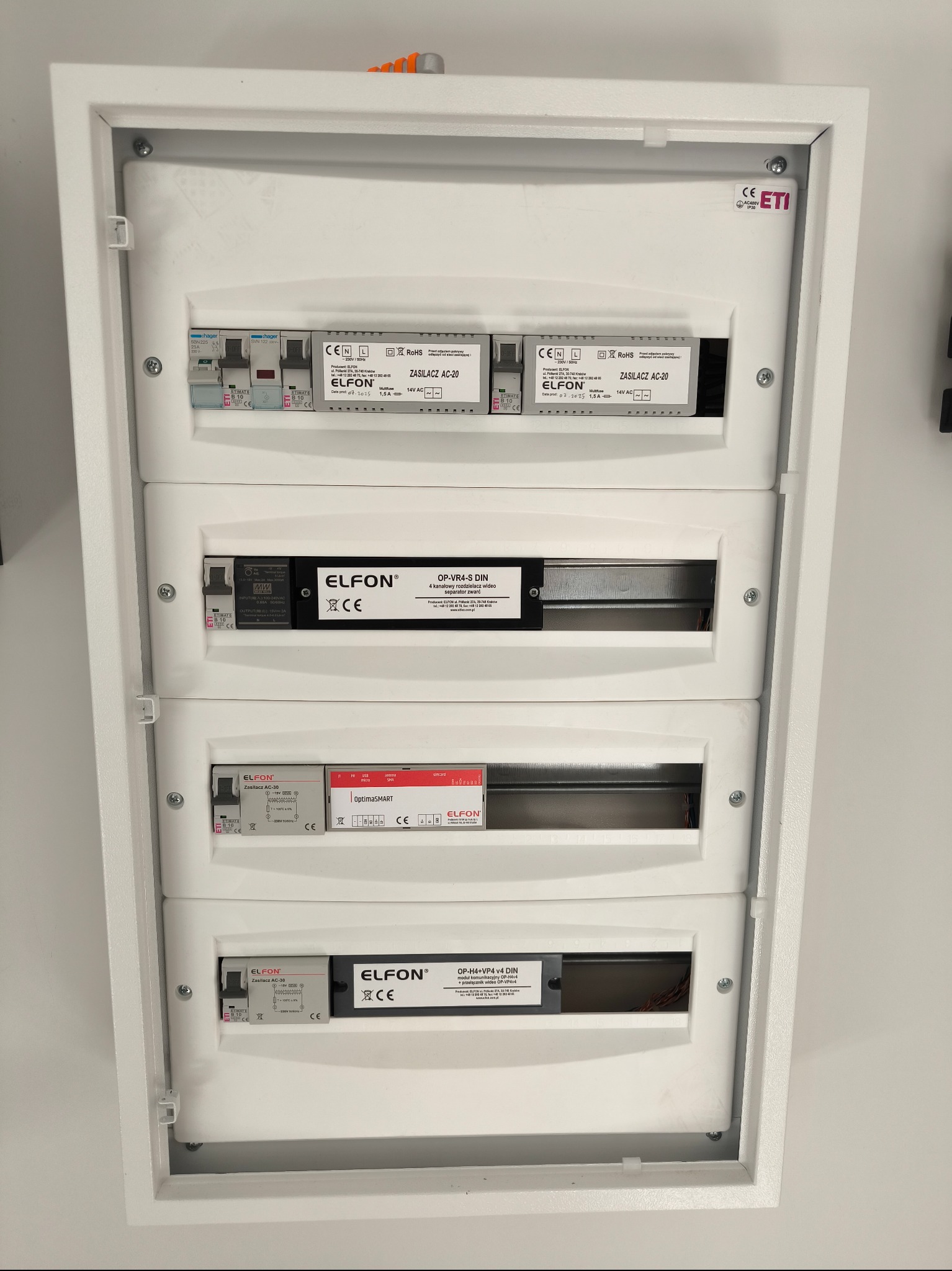 Rozdzielnica elektryczna Elfon w białej obudowie, z widocznymi zabezpieczeniami Hager i modułami Elfon Zasilacz AC-20, OP-VR4-S DIN, OptimaSMART i OP-H4+VP4 v4 DIN.