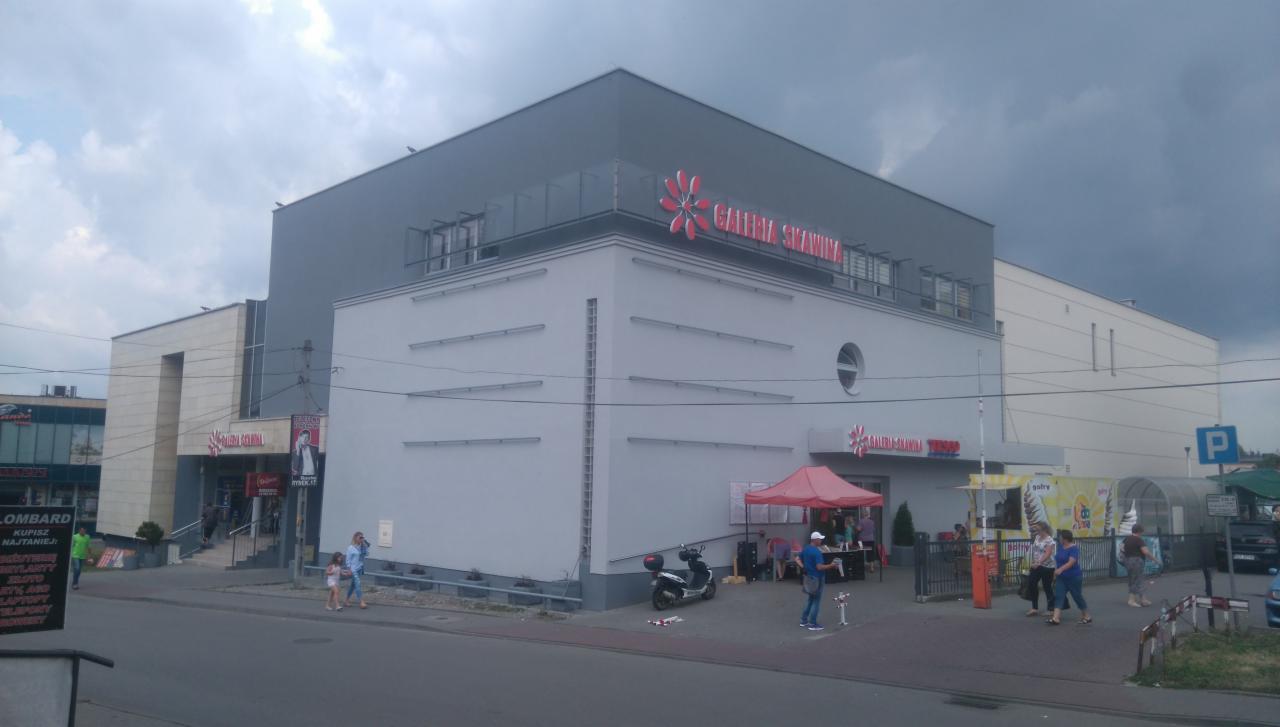 Budynek Galerii Skawina w Mogilanach z szarą elewacją i czerwonym logo, widoczny z ulicy w pochmurny dzień.