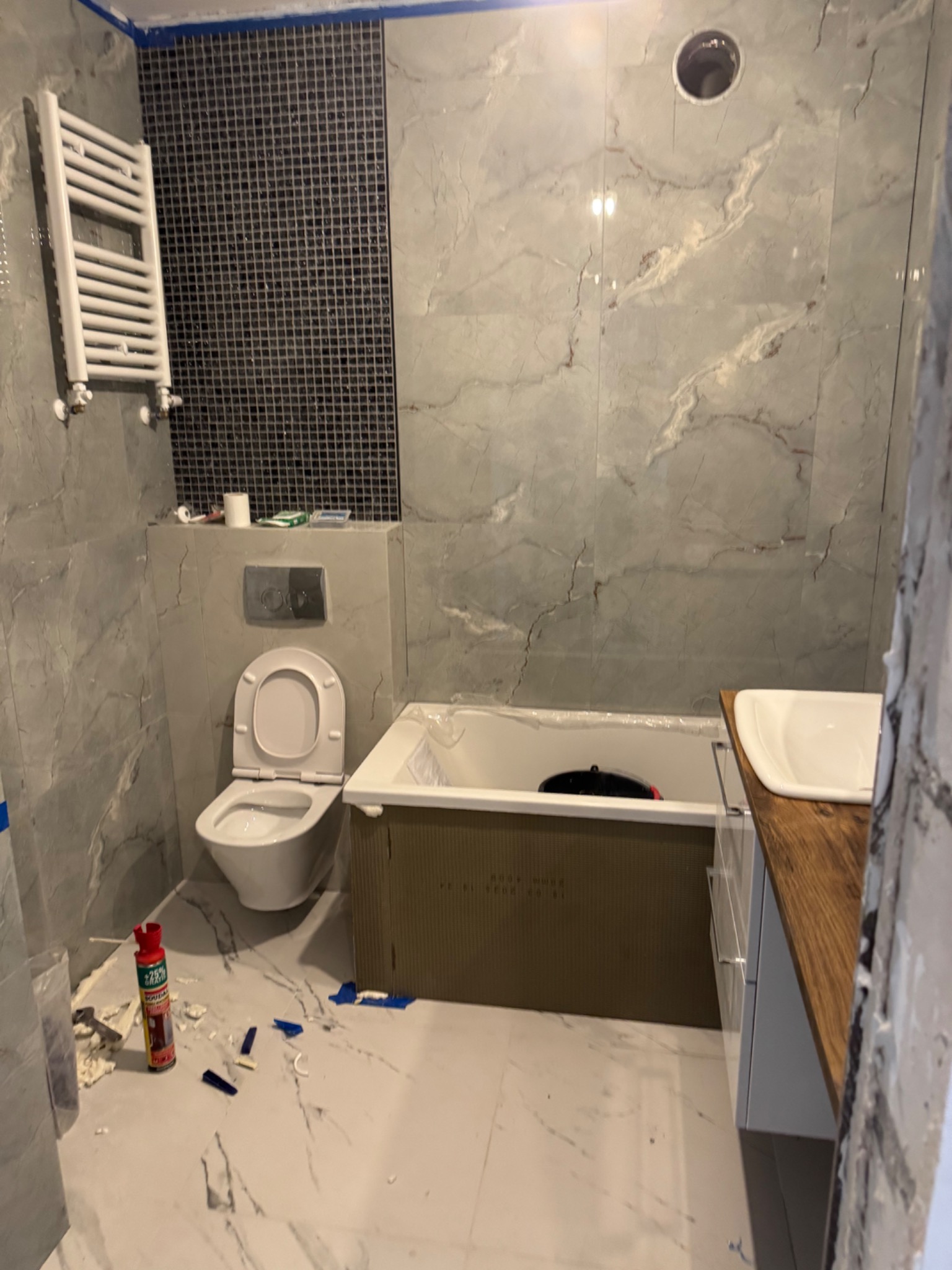 Łazienka w trakcie prac wykończeniowych: marmurowe płytki, mozaika, biała armatura, zabudowa wanny. Widoczne narzędzia i akcesoria instalacyjne.