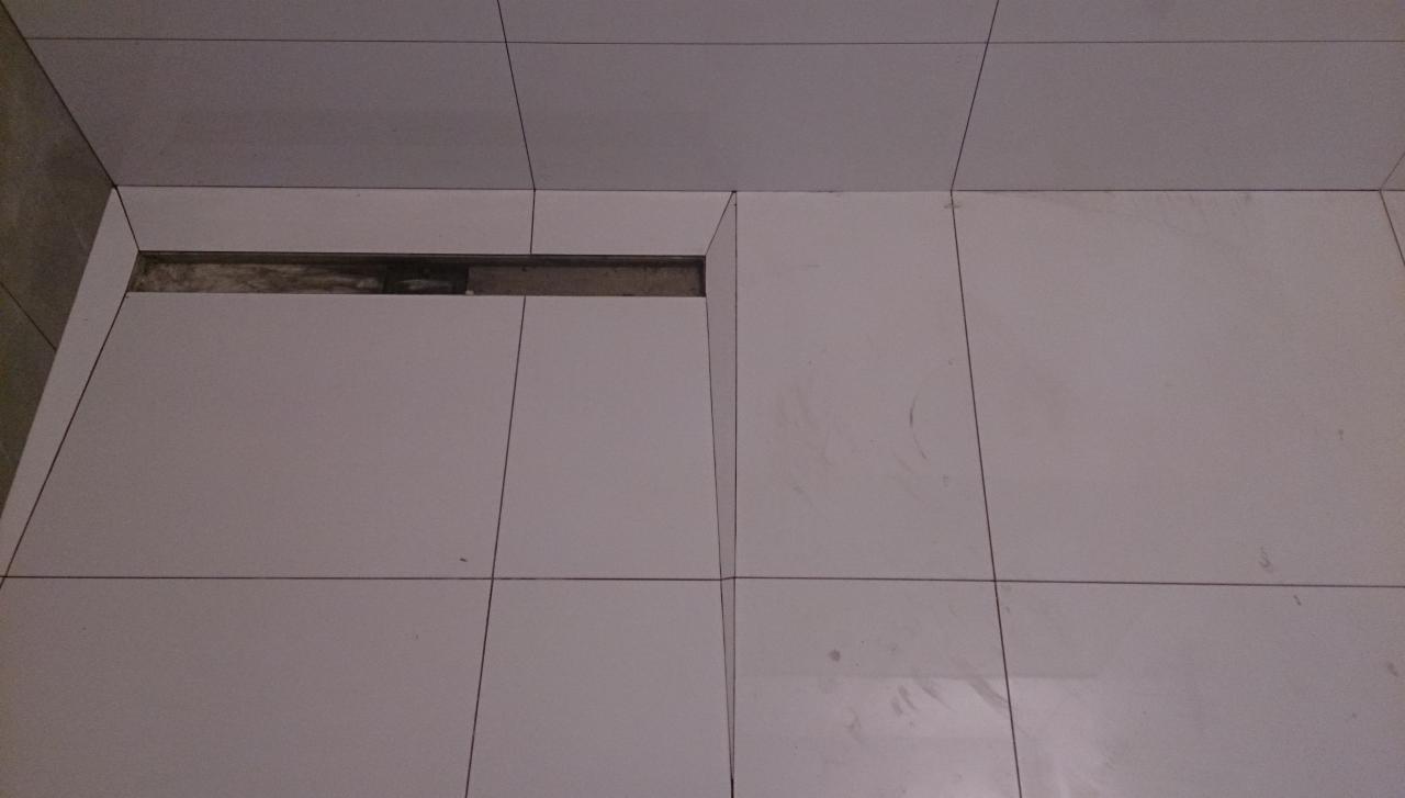 Białe płytki podłogowe w łazience z widocznym odpływem liniowym. Minimalistyczny design, precyzyjne ułożenie płytek. Detal wykończenia podłogi.