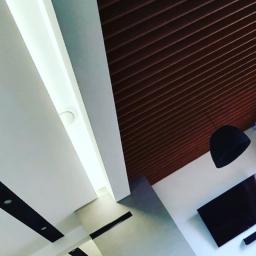 Usługi budowlane Makowski - Nowoczesne wnętrze z brązowym, lamelowym sufitem, oświetleniem LED i minimalistyczną lampą wiszącą, widziane z perspektywy ukośnej.