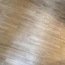 Usługi budowlane Makowski - Ułożone pod kątem beżowe płytki podłogowe imitujące drewno, widoczne delikatne zabrudzenia na powierzchni.