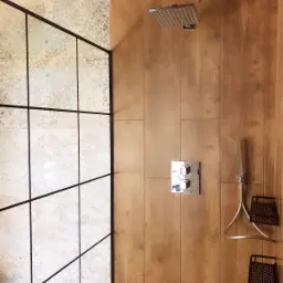 Nowoczesna kabina prysznicowa z deszczownicą i drewnopodobnymi płytkami, wyposażona w termostat i p&oacute;łki na kosmetyki
