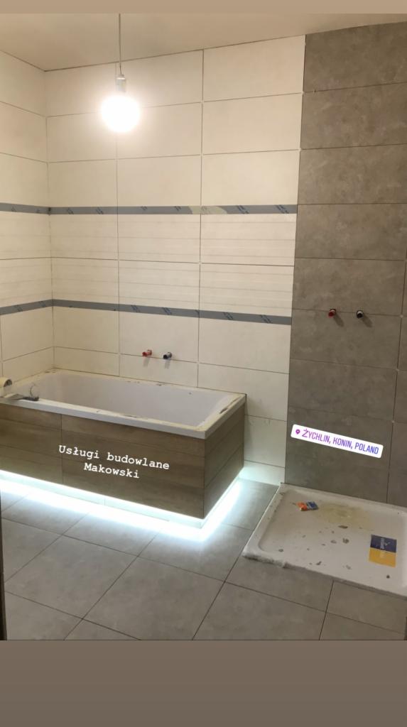 Wnętrze łazienki w trakcie remontu: obudowana wanna z podświetleniem LED, częściowo wykończone płytki ścienne w dwóch odcieniach, brodzik z widocznymi zabrudzeniami po remoncie.