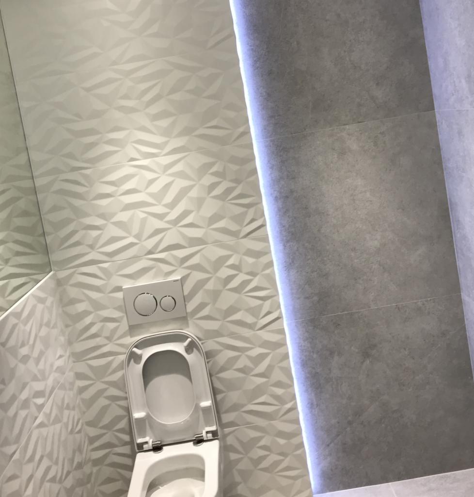 Nowoczesna toaleta z otwartą klapą, białe trójwymiarowe płytki na ścianie i podświetlenie LED w rogu