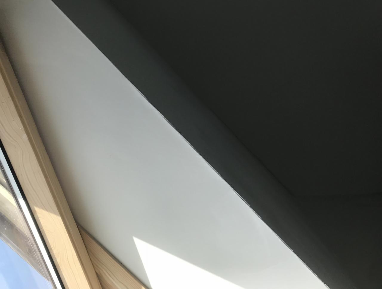 Wnętrze okna dachowego po umyciu, widoczna czysta, biała powierzchnia ramy i szyby, kontrastująca z ciemnym sufitem.