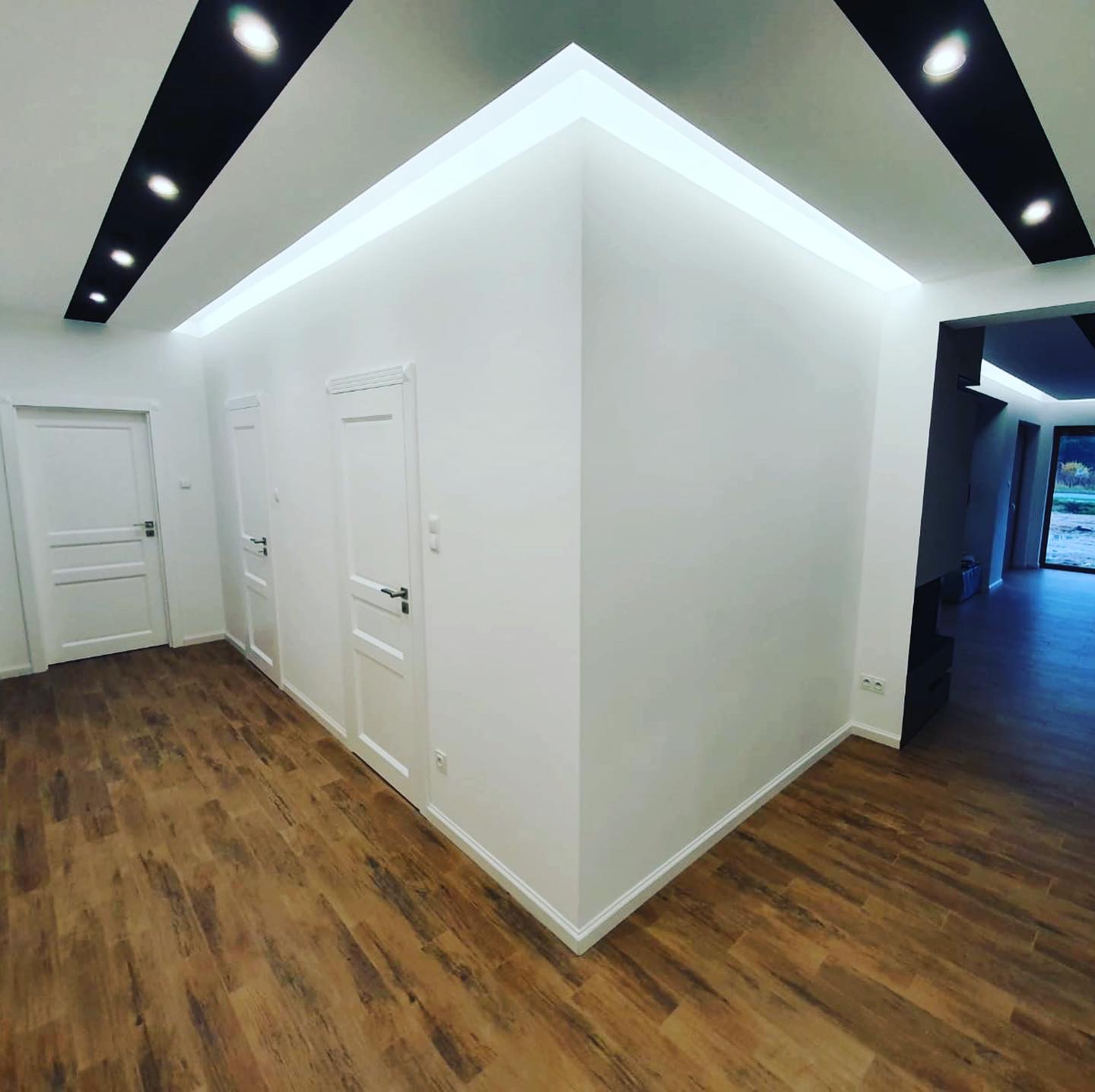 Wnętrze po remoncie w Kazimierzu Biskupim: świeżo umyta podłoga z paneli imitujących drewno, białe ściany i drzwi, nowoczesne oświetlenie sufitowe.