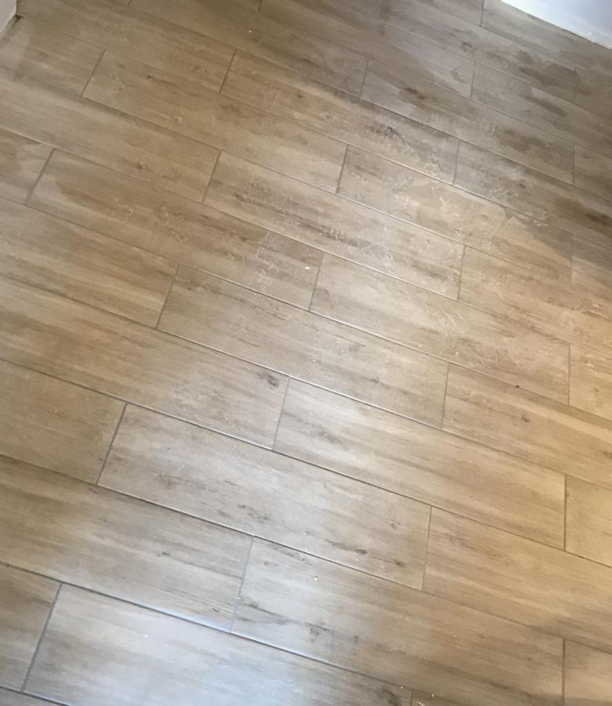 Ułożone pod kątem beżowe płytki podłogowe imitujące drewno, widoczne delikatne zabrudzenia na powierzchni.