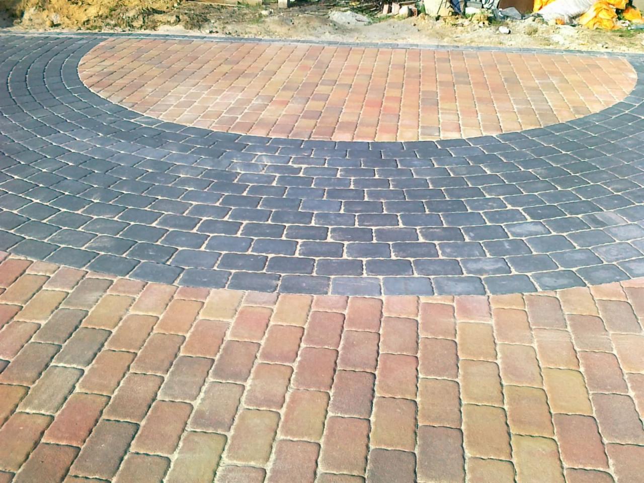 Ułożona kostka brukowa w odcieniach brązu i szarości, tworząca łukowaty wzór. Widoczne połączenie kolorów i faktur kostki.