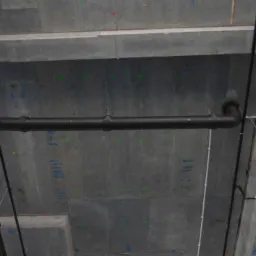 Rurociąg z czarnych rur w surowym, betonowym wnętrzu, z widocznymi kolorowymi oznaczeniami na suficie i ścianach.