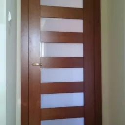 Nowoczesne drzwi wewnętrzne z drewnianą ramą i mlecznymi szybami, zamontowane w Pęgowie, widoczne w korytarzu z jasnymi ścianami.