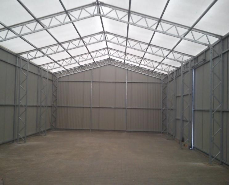 Wnętrze hali stalowej z widoczną konstrukcją nośną i panelami ściennymi. Hala oświetlona naturalnym światłem, posadzka betonowa. Widok na pustą przestrzeń wewnątrz hali.