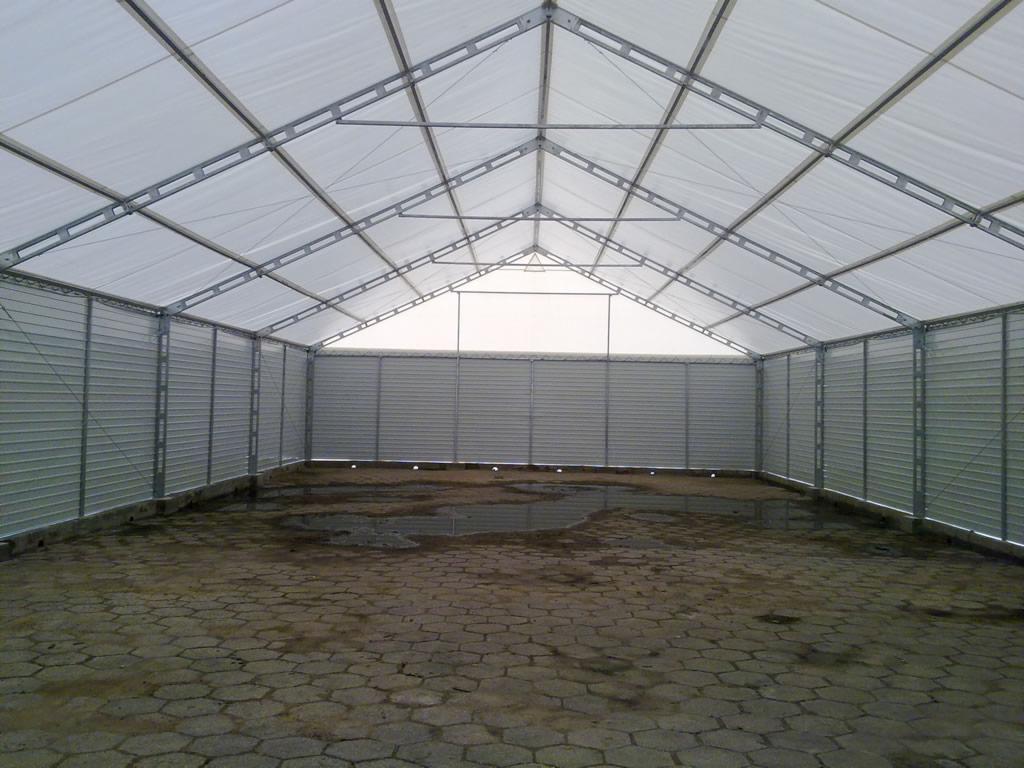 Wnętrze hali z metalową konstrukcją i panelami ściennymi. Na podłodze widoczne kałuże. Konstrukcja dachu z białym poszyciem. Widok z poziomu podłogi.