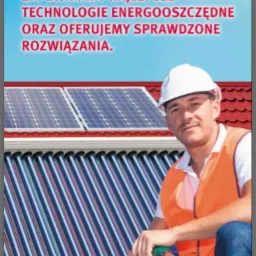 Mężczyzna w kasku i kamizelce odblaskowej, kuca na dachu z czerwonej dachówki obok kolektorów słonecznych, trzymając wiertarkę; w tle widoczne panele fotowoltaiczne; na górze reklama firmy z logo...