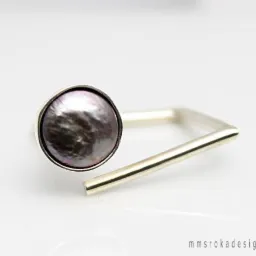 Srebrny pierścionek z okrągłym, opalizującym kamieniem na białym tle, minimalistyczny design.