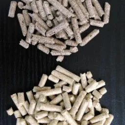 Dwa rodzaje pelletu drzewnego, jaśniejszy i ciemniejszy, ułożone w oddzielnych kupkach na czarnym, lekko połyskującym tle.