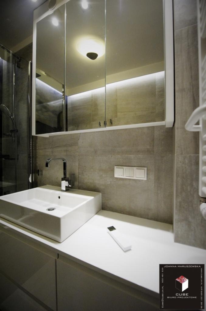 Nowoczesna łazienka: biała, kwadratowa umywalka z chromowaną baterią na tle szarych płytek i lustrzanej szafki z oświetleniem LED.