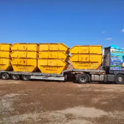 Ciężarówka z żółtymi kontenerami firmy Krynicki Recykling na tle błękitnego nieba. Na kabinie reklama fotowoltaiki. Transport odpadów budowlanych.