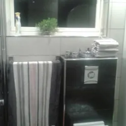 Nowoczesna łazienka z podwieszaną toaletą, ciemną zabudową, jasnymi płytkami i oknem z rośliną. Ręcznik w paski na relingu. Minimalistyczny design.