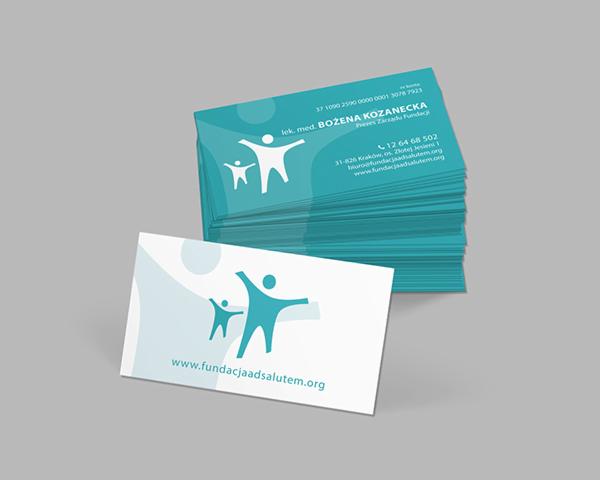 Stos wizytówek w odcieniach turkusu i bieli, z logo fundacji przedstawiającym dwie stylizowane postacie i adresem strony internetowej.