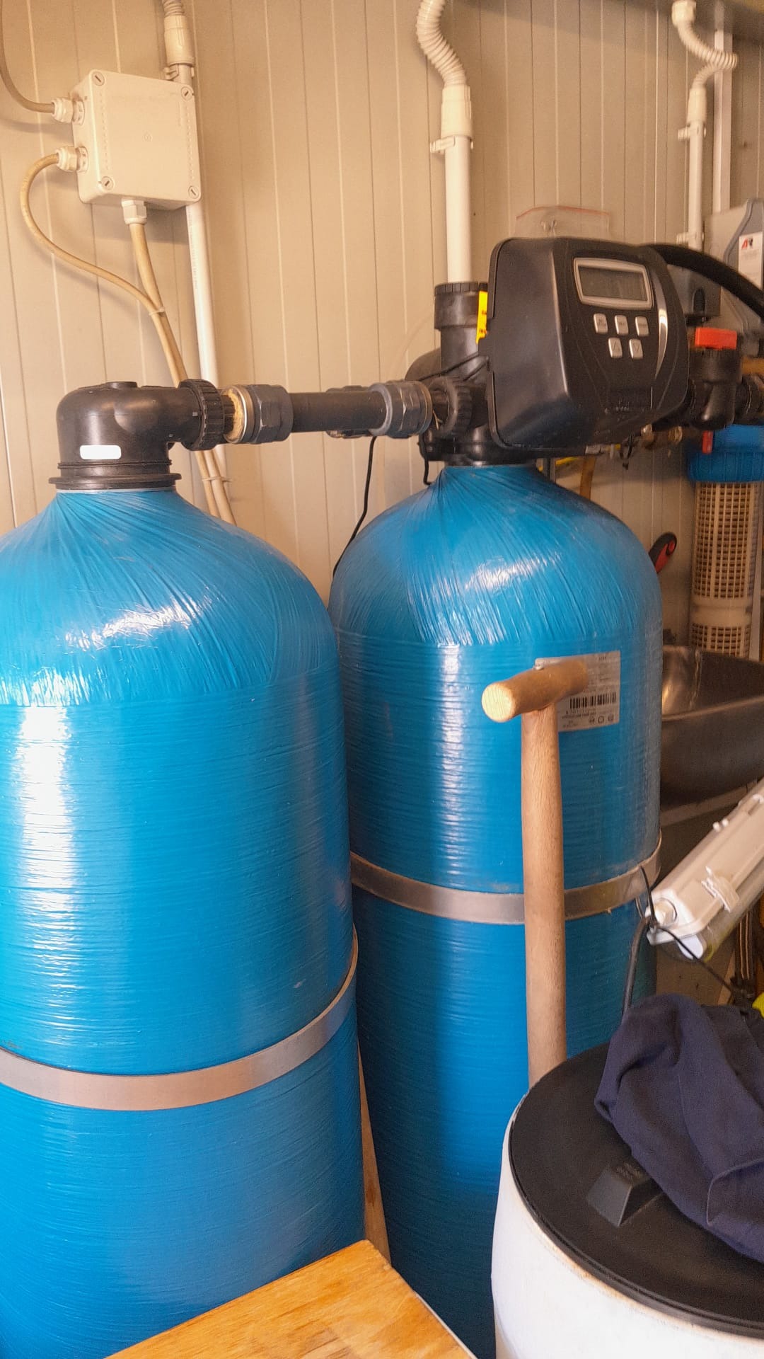 Dwa niebieskie zbiorniki z czarnymi głowicami i rurami w pomieszczeniu. Elementy instalacji uzdatniania wody z widocznymi przewodami i osprzętem.