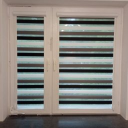 Deco-Light - Dwuskrzydłowe okno z zamontowanymi roletami w dzień noc, z naprzemiennymi pasami w odcieniach szarości i bieli. Widoczne detale mechanizmu rolet.