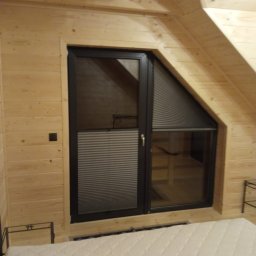 Deco-Light - Okno dachowe z zamontowaną plisowaną przesłoną w drewnianej obudowie poddasza. Plisa częściowo zasłonięta, widoczna faktura materiału.