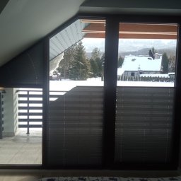 Deco-Light - Zaciemniające plisowane osłony okienne w szarej tonacji, dopasowane do nietypowego kształtu okna na poddaszu, z widokiem na zimowy krajobraz.