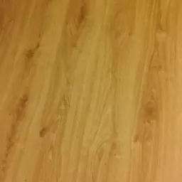 Jasny parkiet laminowany ułożony wzdłuż zielonej ściany z listwami przypodłogowymi. Widok z góry, ciepłe oświetlenie, imitacja drewna.